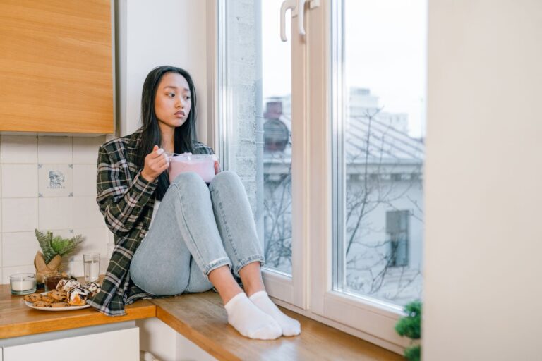 sad woman sitting on kitchen counter while eating ice cream